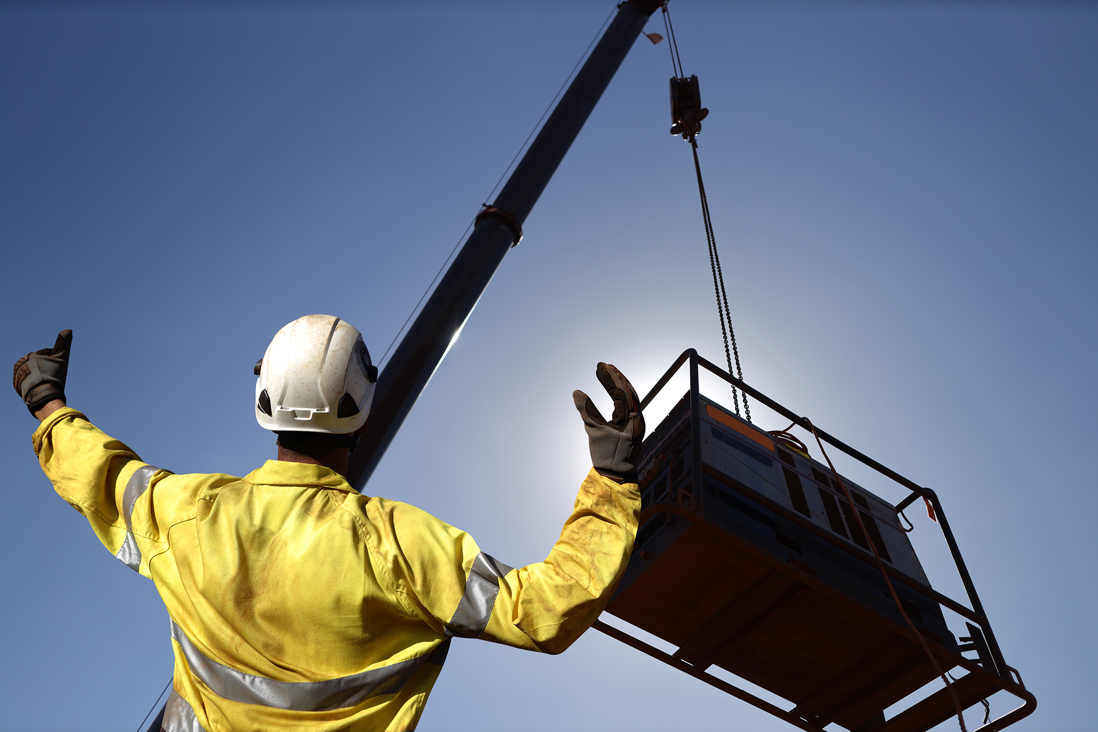 spotter in ppe guiding a shipping container on a crane